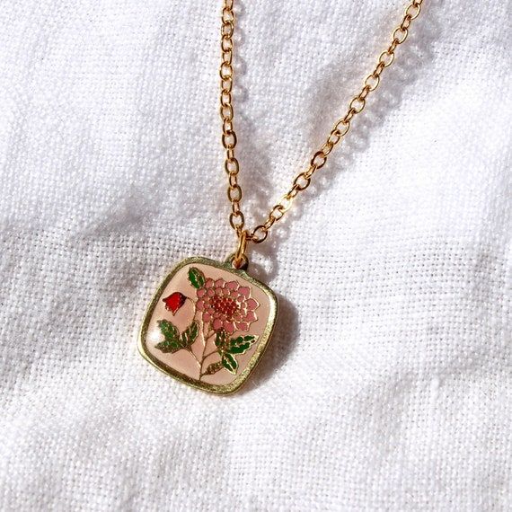 Vintage guldhalsband med blommigt emaljhänge mot vit bakgrund.